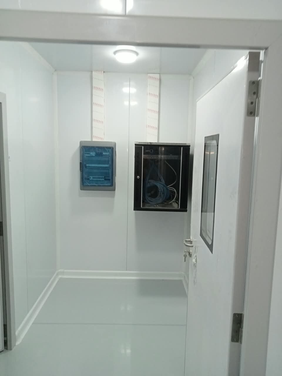 Salle blanche avec porte à hublot, tableau électrique et baie informatique